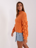 Didelis oranžinis megztinis su storu pynimu.
