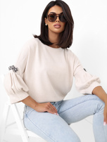 Helle beige Damenpullover mit Applikationen an den Ärmeln.