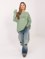 Pistazienfarbener Oversize-Pullover mit kontrastierendem Schriftzug.