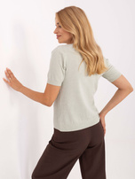 Pistazienfarbener Pullover mit dekorativer Kette.
