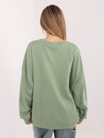 Pistazienfarbener Oversize-Pullover mit kontrastierendem Schriftzug.